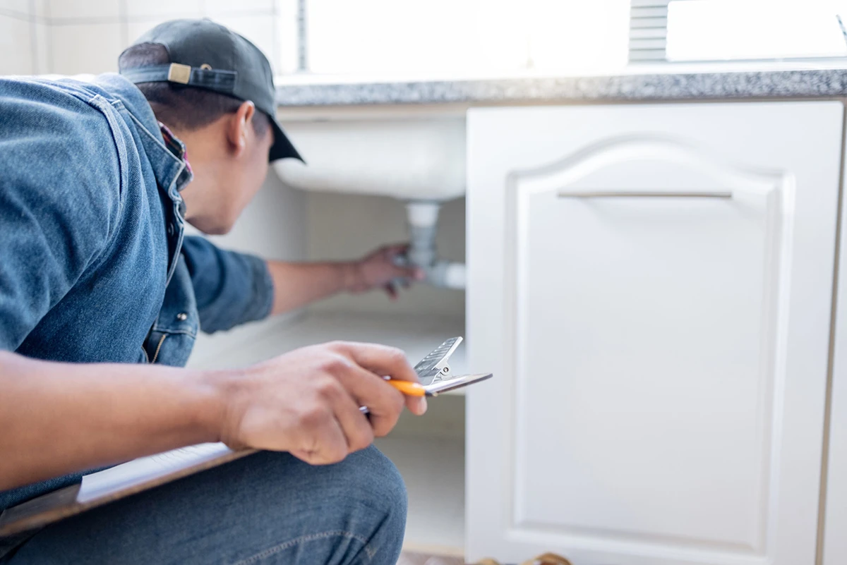 Plumbing technician inspecting pipes under a kitchen sink